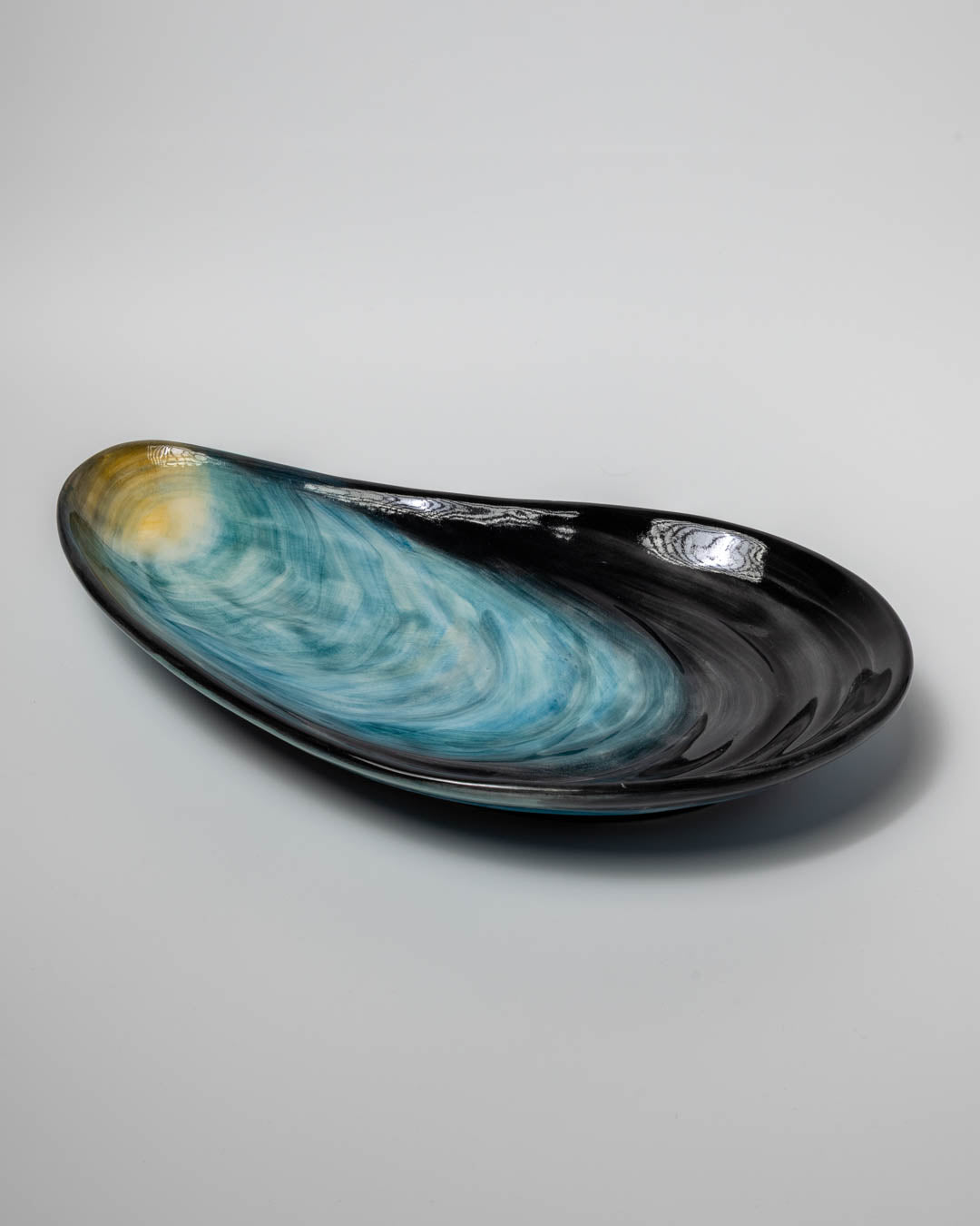 Decorative ceramics serving plate with black and blue design like a blue mussel shell on a gray background